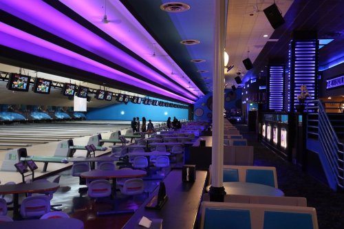 A vibrant bowling alley with purple lighting, empty lanes, and seating areas, creating a lively atmosphere.