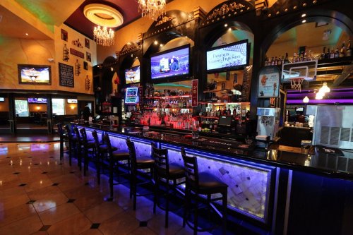 A vibrant bar with illuminated seating, multiple TVs, and a colorful decor in a lively atmosphere.