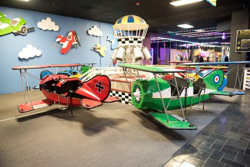 Colorful biplane rides in an amusement area, with a whimsical control tower and cloud decorations in the background.