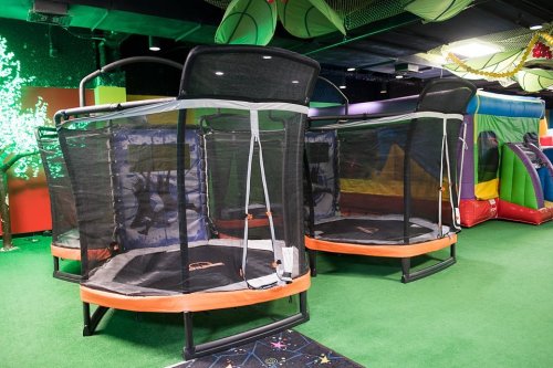 Two enclosed trampolines on a green floor in a colorful indoor play area.
