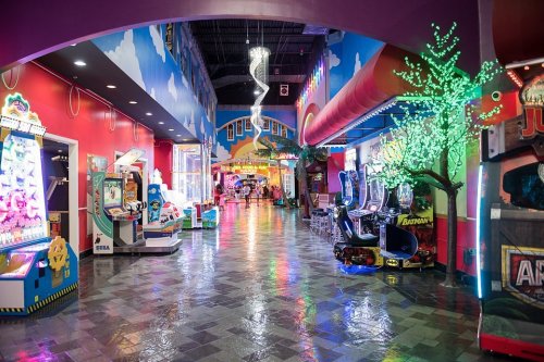 Colorful arcade hallway with game machines, vibrant decor, and reflective floors under bright lights.