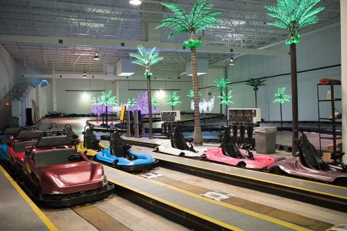 Indoor go-kart track featuring colorful karts and illuminated palm trees in a spacious venue.