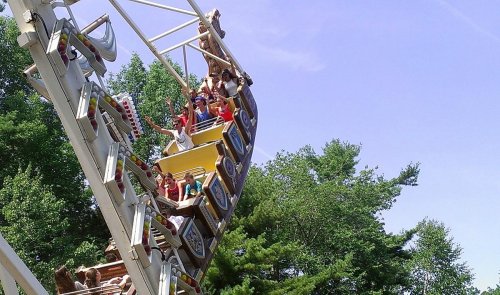 A group of people enjoying a thrilling ride on a amusement park attraction against a clear blue sky and green trees.