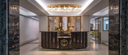 Elegant hotel lobby with a marble reception desk, decorative lighting, and stylish seating areas in the background.
