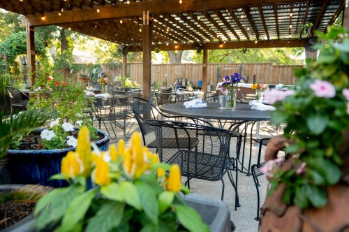A charming outdoor dining area with tables, flowers, and a wooden pergola, creating a cozy atmosphere.