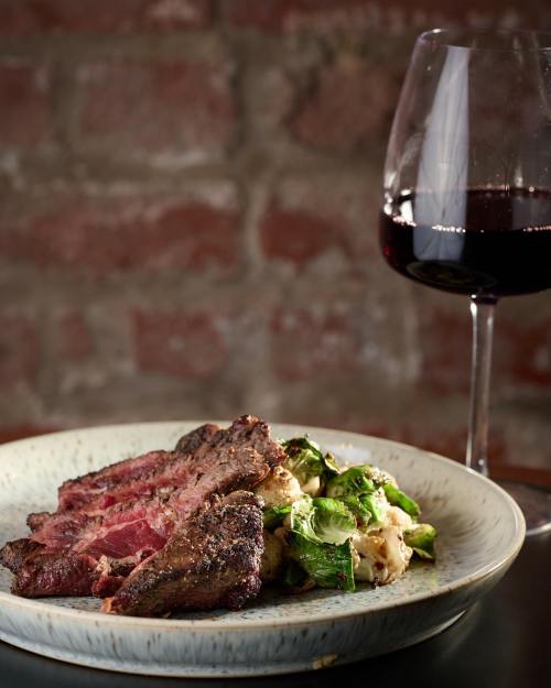A plate of sliced steak with Brussels sprouts and cauliflower, accompanied by a glass of red wine.