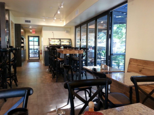 Interior of a cozy restaurant with wooden tables, chairs, and large windows letting in natural light.