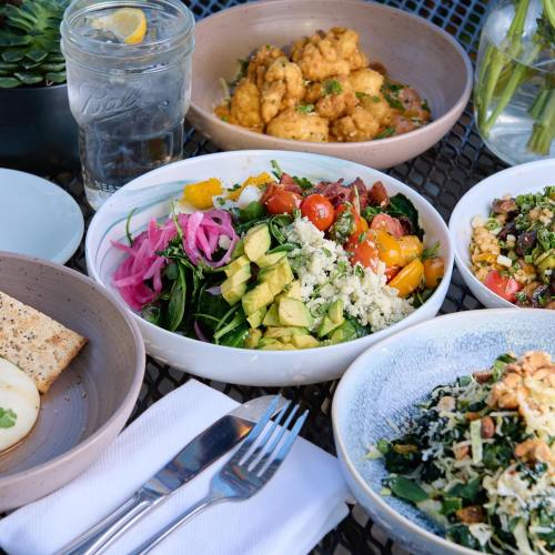 A table setting with colorful salads, cauliflower bites, and drinks, surrounded by greenery.