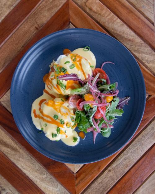 A blue plate with poached eggs topped with hollandaise sauce, served with a fresh salad of greens and tomatoes.