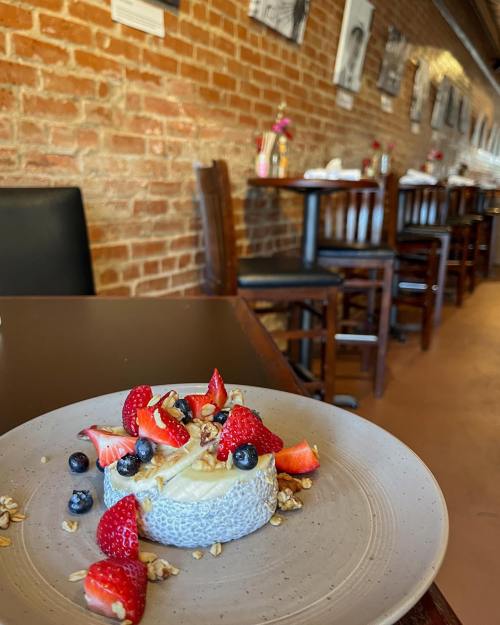 A dessert plate with a creamy base topped with strawberries, blueberries, and granola, set in a cozy restaurant.