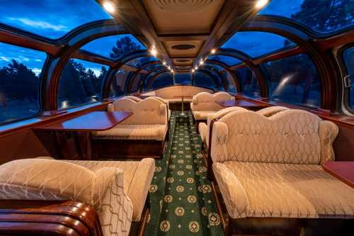 Interior of a vintage train car featuring plush seating, elegant decor, and large windows under a twilight sky.