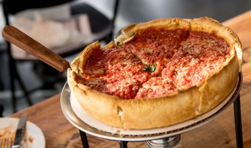 A freshly baked deep-dish pizza with a golden crust and rich tomato sauce, served on a wooden table.