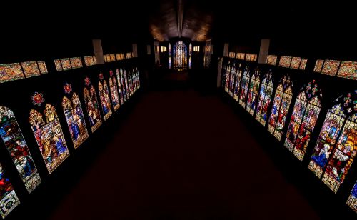 A dimly lit corridor lined with colorful stained glass windows depicting various scenes.