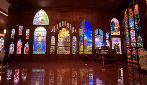 A beautifully lit room featuring colorful stained glass windows and an organ, reflecting on polished floors.