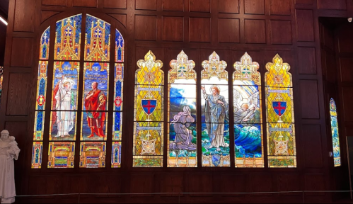 Stained glass windows depicting biblical scenes, framed by dark wood, in a church interior.