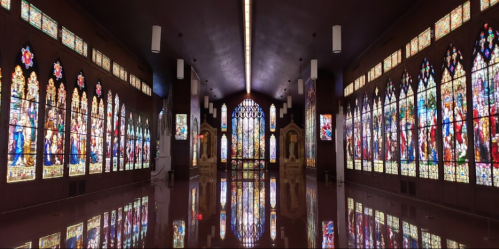 A panoramic view of a church interior featuring colorful stained glass windows and a reflective floor.