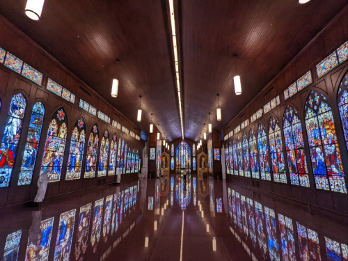 A spacious hall with colorful stained glass windows reflecting on a polished floor, illuminated by overhead lights.