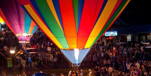 Colorful hot air balloons illuminate the night sky above a crowded festival scene.