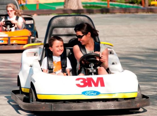 A woman and a child smile while riding in a go-kart on a racetrack.