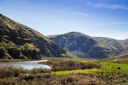 A serene river winding through lush green hills under a clear blue sky.