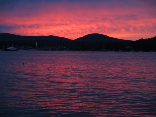 A vibrant sunset casts pink and purple hues over a calm lake, with silhouettes of mountains in the background.