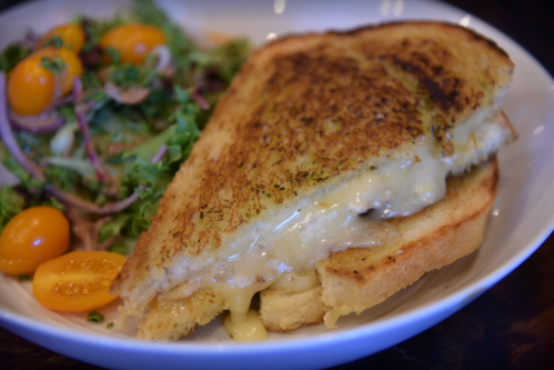 A golden-brown grilled cheese sandwich with melted cheese, served alongside a fresh salad and cherry tomatoes.