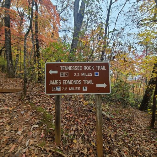 Trail sign indicating Tennessee Rock Trail (2.2 miles) and James Edmonds Trail (7.2 miles) surrounded by autumn foliage.