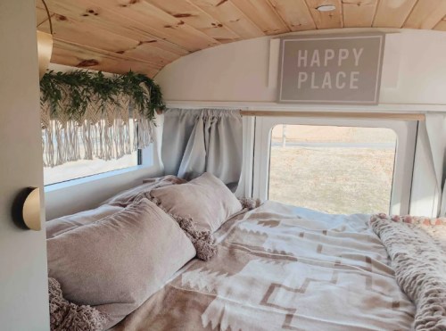 Cozy interior of a camper van featuring a bed with plush pillows, a warm blanket, and a sign that says "Happy Place."