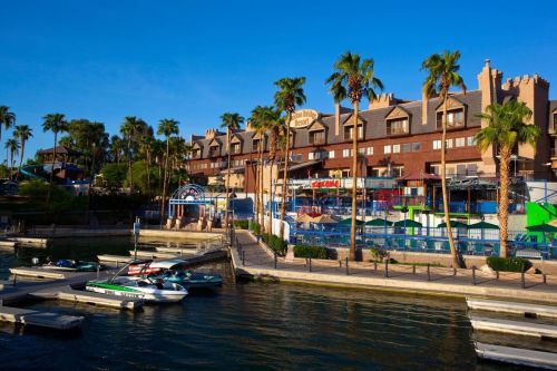 A waterfront view of a hotel with palm trees, boats docked, and clear blue skies.