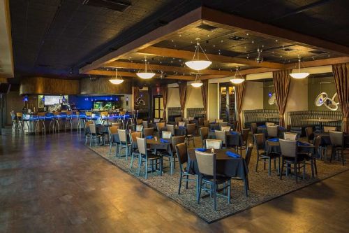 A spacious restaurant interior with tables set for dining, a bar area, and warm lighting.