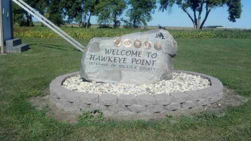 A large stone monument with "Welcome to Hawkeye Point" and "Veterans of Oskaloosa County" engraved, surrounded by landscaping.