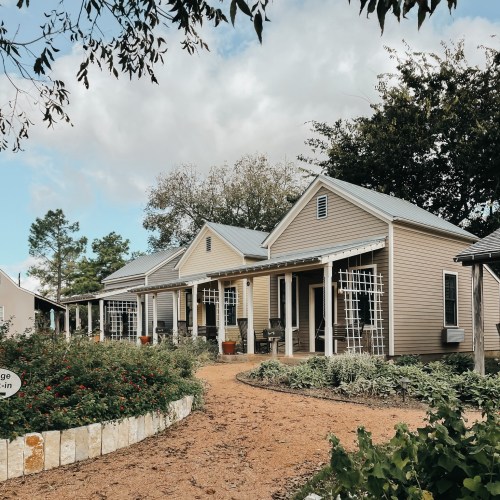 A row of charming, light-colored cottages with porches, surrounded by greenery and a winding path.