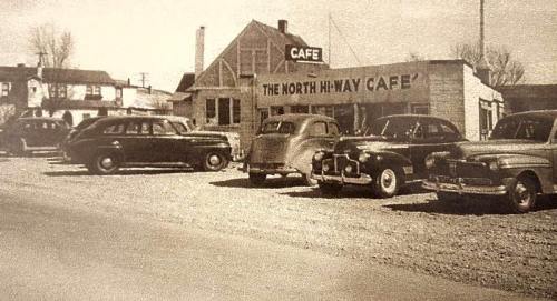 Black and white photo of vintage cars parked outside the North Hi-Way Café, a roadside diner.