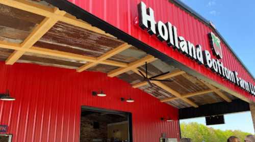 Exterior of Holland Bottom Family Farm building with a red metal facade and wooden accents. Bright and inviting atmosphere.