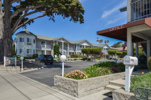 A well-maintained apartment complex with landscaped gardens, parking, and an office entrance.