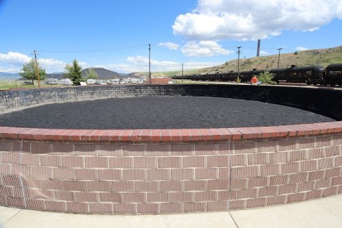 A circular coal storage area with a brick wall, surrounded by a landscape of hills and blue sky with clouds.