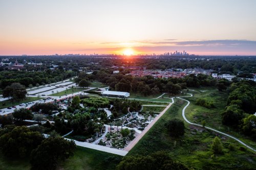 Aerial view of a park at sunset, with city skyline in the background and lush greenery in the foreground.