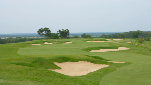 A scenic golf course with lush green fairways and sand bunkers under a cloudy sky.