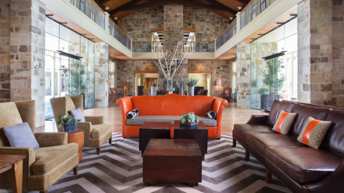 Modern lobby with stone walls, wooden beams, and stylish seating, featuring an orange sofa and a zigzag patterned rug.