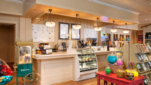 A cozy café interior featuring a display case, coffee station, and colorful candy jars on a red table.