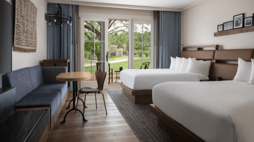A modern hotel room featuring two beds, a seating area, and large windows overlooking a green landscape.