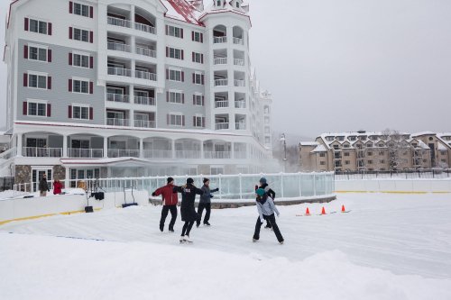 People ice skating in front of a large hotel, surrounded by snow and winter scenery.
