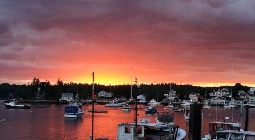 A vibrant sunset over a harbor filled with boats, with colorful clouds reflecting on the water.