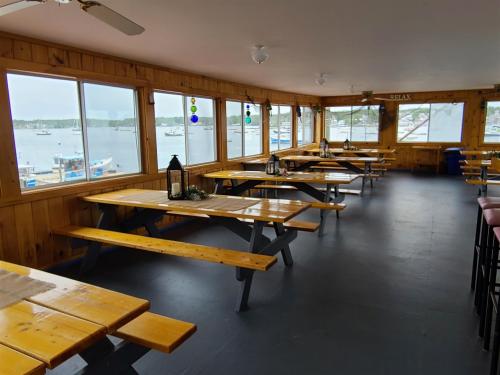 Interior of a waterfront restaurant with wooden tables, large windows, and a view of boats outside.