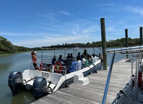 A group of people on a boat at a dock, surrounded by water and trees under a clear blue sky.