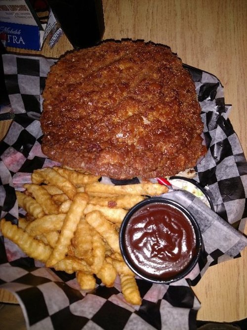 A large, crispy fried chicken sandwich with crinkle-cut fries and a side of barbecue sauce on a checkered paper.