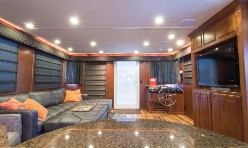 A stylish lounge area with a sectional sofa, wooden cabinetry, a TV, and a foosball table, illuminated by recessed lighting.