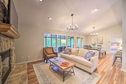Cozy living room with a stone fireplace, comfortable seating, and large windows overlooking greenery.