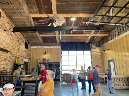 Interior of a casual dining space with people in line, wooden decor, and a large fan overhead.