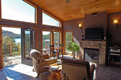 Cozy living room with large windows, a fireplace, and a view of the lake, featuring comfortable seating and a dining area.